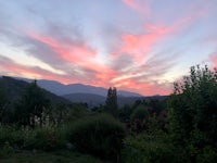 a pink sunset over a garden with mountains in the background