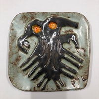 a square ceramic plate with a black and orange design